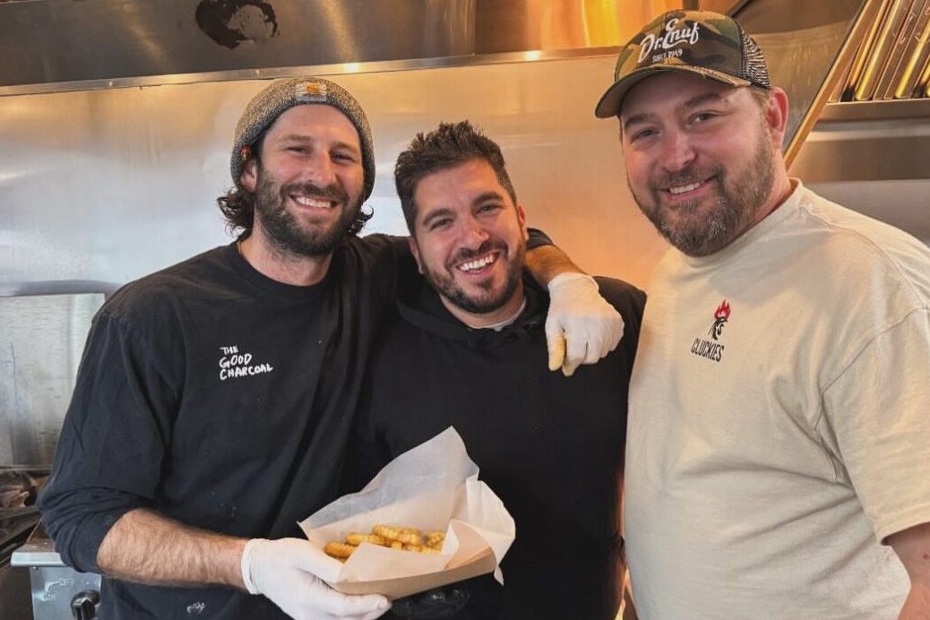 The Cluckies Hot Chicken crew smiling in the kitchen with a tray of fries